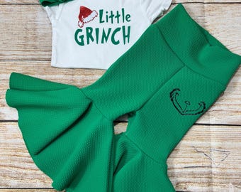 May include: A green and white baby outfit with a green headband, a white onesie with the text "Little Grinch" and a green Santa hat graphic, and green bell bottom pants with a green Santa hat graphic.