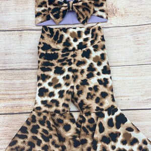 May include: A brown and white leopard print baby girl's outfit with a lavender bow headband.
