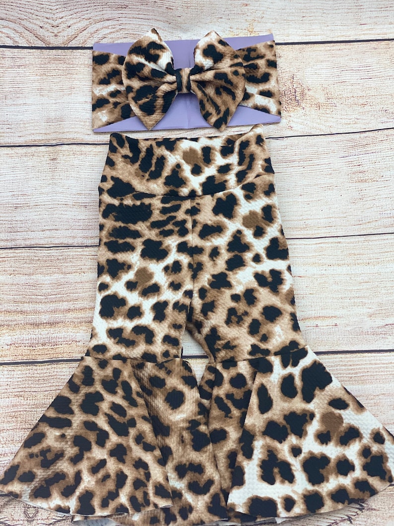 May include: A brown and white leopard print baby girl's outfit with a lavender bow headband.