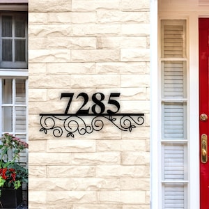 May include: Black metal house number plaque with a decorative scroll design. The numbers 7285 are displayed on the plaque.