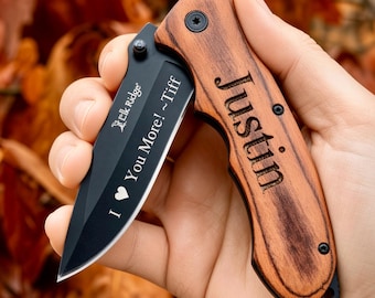 May include: A folding pocket knife with a black blade and a wood grain handle. The blade features the text "Elk Ridge" and "I ♥ You More! ~Tiff" in white. The wooden handle is engraved with the name "Justin" in a dark, bold font.