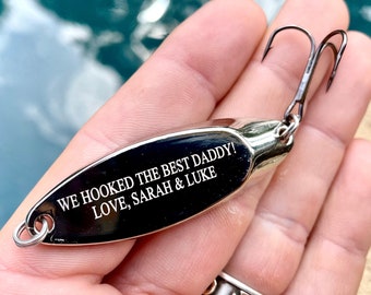 Puede incluir: Señuelo de pesca plateado con una inscripción negra que dice "We hooked the best daddy! Love, Sarah & Luke"