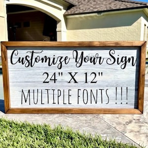 May include: A rectangular wooden sign with a light gray background and a brown frame. The sign reads "Customize Your Sign" in cursive, with the dimensions "24" X 12"" and "MULTIPLE FONTS !!!" in a bold font.