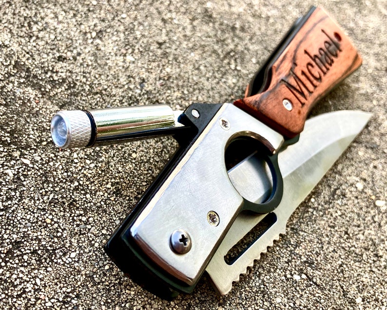 May include: A personalized pocket knife with a wooden handle engraved with the name "Michael". The knife has a silver blade and a built-in flashlight.