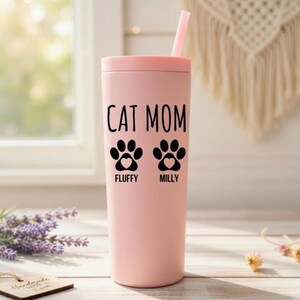 K&ouml;nnte beinhalten: Ein rosa Becher mit Deckel und Strohhalm. Auf dem Becher stehen die schwarzen Worte "CAT MOM" sowie zwei Pfotenabdr&uuml;cke mit Herzen. Unter den Pfotenabdr&uuml;cken stehen die Namen "Fluffy" und "Milly".