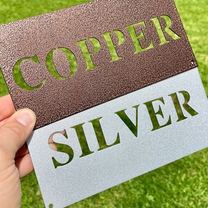 May include: A metal sign with the words "COPPER" and "SILVER" in a contrasting color scheme. The top portion of the sign is a copper color with the word "COPPER" cut out in a lighter color. The bottom portion of the sign is a silver color with the word "SILVER" cut out in a darker color.