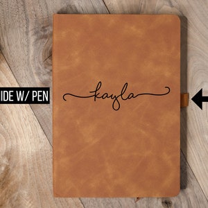May include: A brown leather journal with the name "kayla" in cursive script. The journal has a ribbon bookmark and the text "RAWHIDE W/ PEN". The cover has a textured appearance.