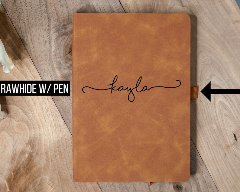 May include: A brown leather journal with the name "kayla" in cursive script. The journal has a ribbon bookmark and the text "RAWHIDE W/ PEN". The cover has a textured appearance.