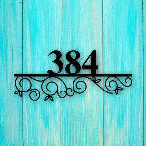 May include: Black metal house number sign with the number 384 on a turquoise wooden background. The number is attached to a decorative scrollwork design.