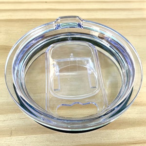 May include: Clear plastic lid for a travel mug with a silicone ring around the edge. The lid has a small opening for sipping and a larger opening for adding ice.