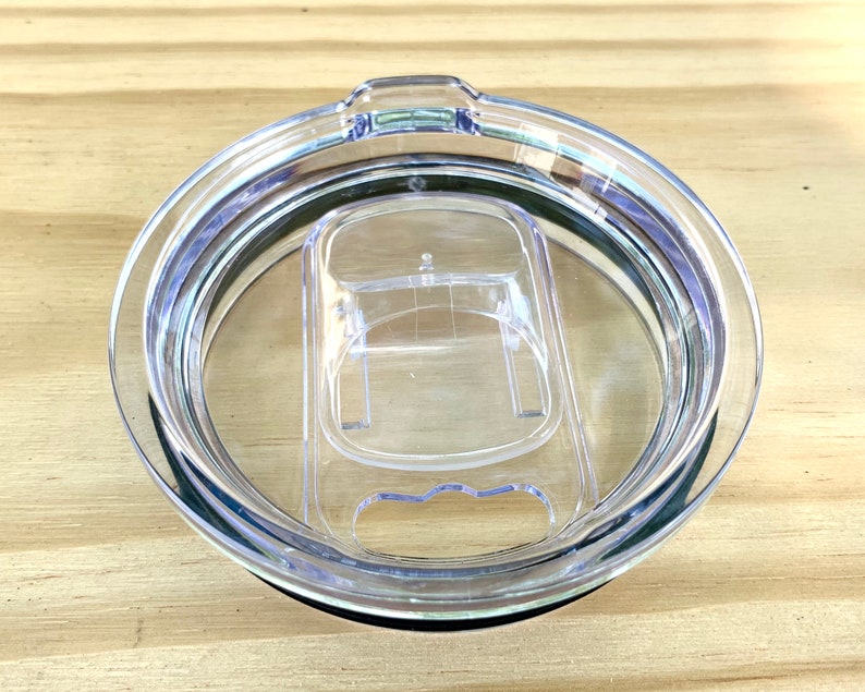 May include: Clear plastic lid for a travel mug with a silicone ring around the edge. The lid has a small opening for sipping and a larger opening for adding ice.
