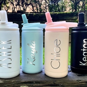 May include: Four personalized water bottles in pastel colors: white, light blue, peach, and black. Each bottle has a name in silver script: Asher, Kayla, Chloe, and Keaton. The bottles have a straw and a flip-top lid.