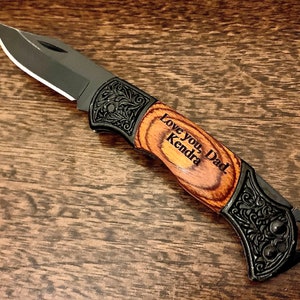 May include: A black pocket knife with a wood handle. The handle is engraved with the words "Love you, Dad. Kendra".