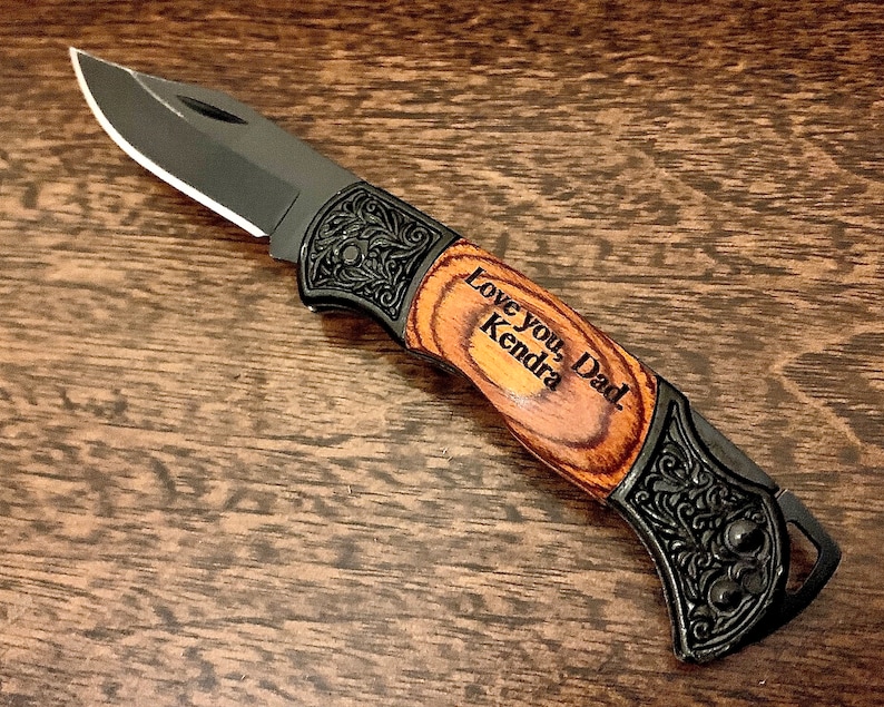 May include: A black pocket knife with a wood handle. The handle is engraved with the words "Love you, Dad. Kendra".