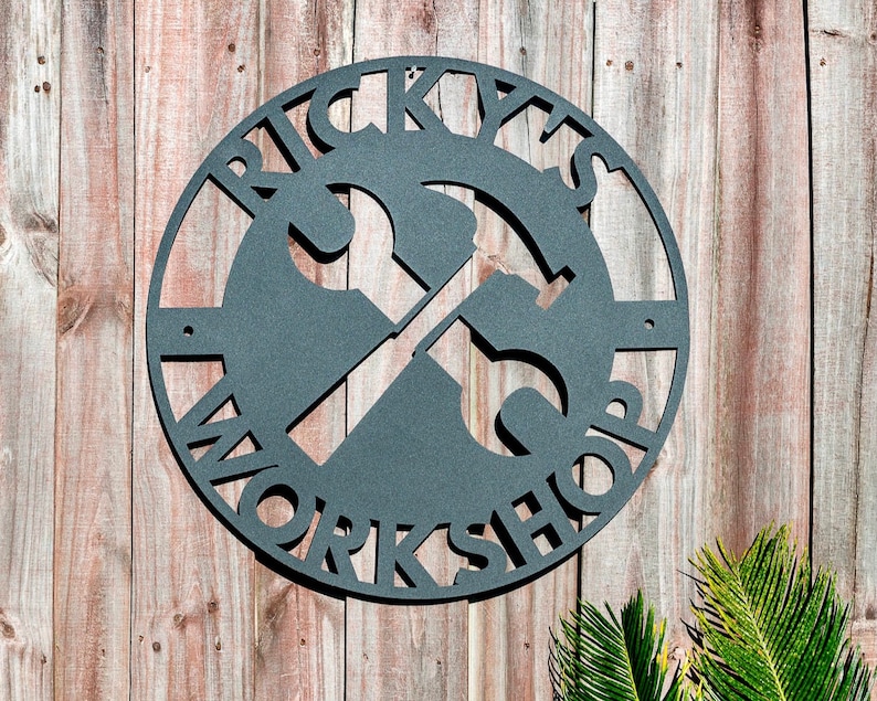 May include: A black metal sign with the words "Ricky's Workshop" in a circle with a wrench and hammer crossed in the center.