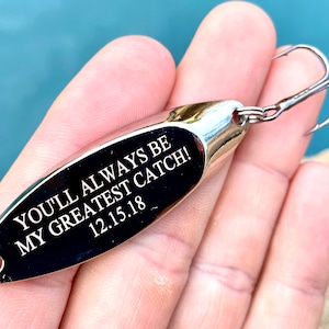 Puede incluir: Se&ntilde;uelo de pesca plateado con una inscripci&oacute;n negra que dice "You'll always be my greatest catch! 12.15.18".