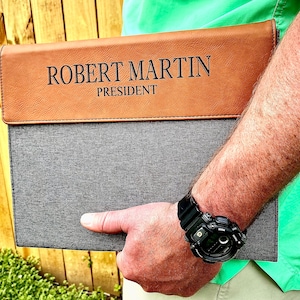 May include: A brown leather and gray fabric portfolio with the name "ROBERT MARTIN PRESIDENT" embossed in black lettering.