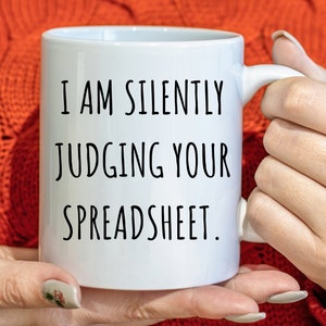May include: White ceramic mug with black text that reads "I am silently judging your spreadsheet."
