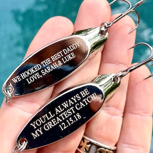 Puede incluir: Dos se&ntilde;uelos de pesca plateados con mensajes grabados. El se&ntilde;uelo superior dice "We hooked the best daddy! Love, Sarah & Luke". El se&ntilde;uelo inferior dice "You'll always be my greatest catch! 12.15.18".