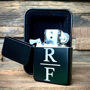 May include: Black lighter with a personalized inscription "R/F" on the front. The lighter is in a black case.