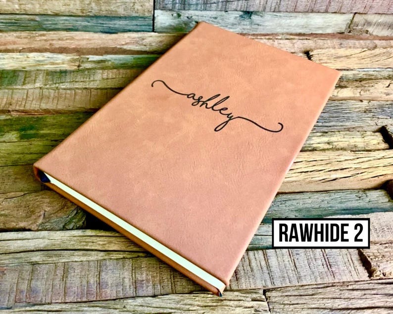 May include: A personalized, light brown journal with the name "ashley" in cursive script. The journal has a gold-colored edge and the text "RAWHIDE 2" in a white box.