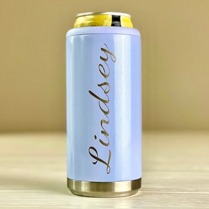 May include: A pale blue can cooler with the name "Lindsey" in gold script. The cooler has silver rims and is designed to hold a standard can. A yellow and white can is inside the cooler.
