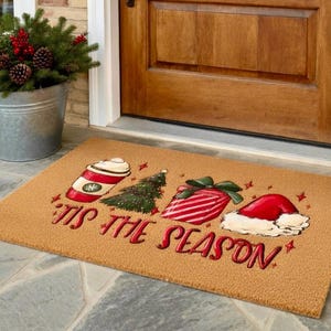 May include: A rectangular doormat with a festive Christmas design. It features a red and white coffee cup, a green Christmas tree, a wrapped gift, and a Santa hat. The words "'Tis the Season" are written in red.