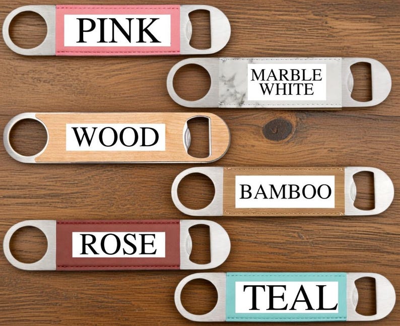 May include: A collection of bottle openers with stainless steel bodies and color-coded inserts. The inserts display the words "PINK", "MARBLE WHITE", "WOOD", "BAMBOO", "ROSE", and "TEAL". The openers are arranged on a wooden surface.