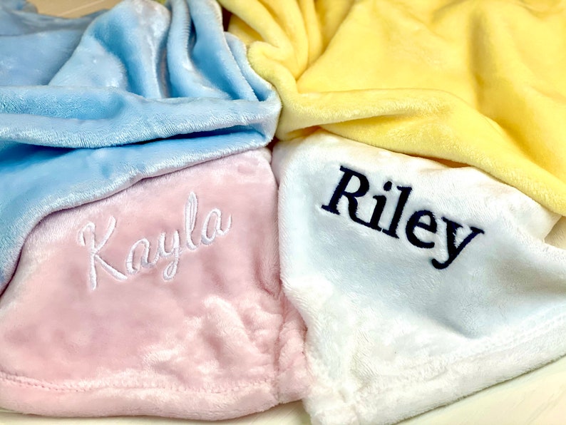 May include: Three personalized plush blankets in pink, white, and blue with the names "Kayla" and "Riley" embroidered on them.