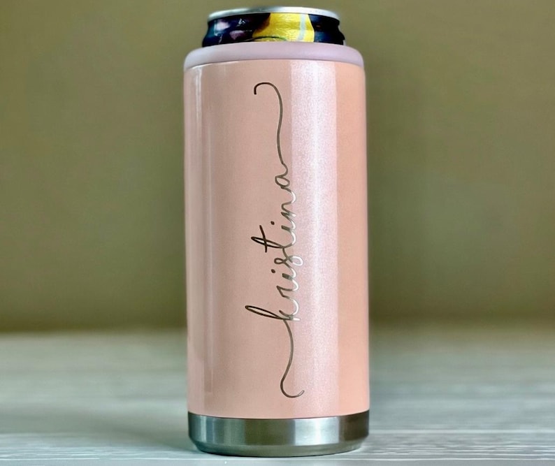 May include: A pale pink insulated can cooler with a silver base and rim. The name "Kristina" is written in a cursive font on the side. The top of the cooler has a light purple rim to hold a can.