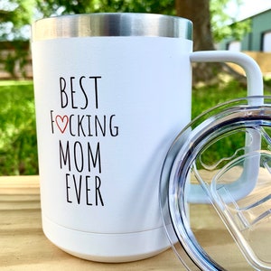 May include: White stainless steel travel mug with a black handle and lid. The mug has the text "BEST F♡CKING MOM EVER" printed on the front.