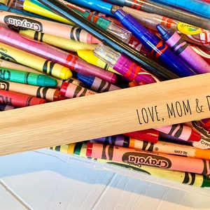 May include: A wooden sign with the text "LOVE, MOM & DAD" on it. The sign is sitting on top of a container filled with colorful crayons.