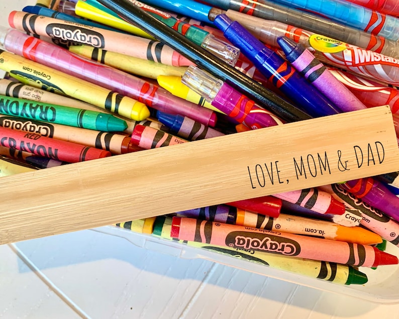 May include: A wooden sign with the text "LOVE, MOM & DAD" on it. The sign is sitting on top of a container filled with colorful crayons.