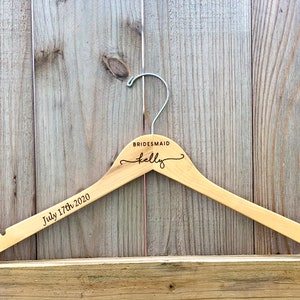 May include: A wooden hanger with the text "BRIDESMAID Kelly" and "July 17th, 2020" engraved on it.