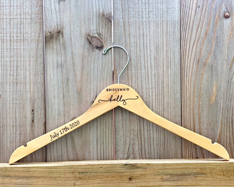 May include: A wooden hanger with the text "BRIDESMAID Kelly" and "July 17th, 2020" engraved on it.