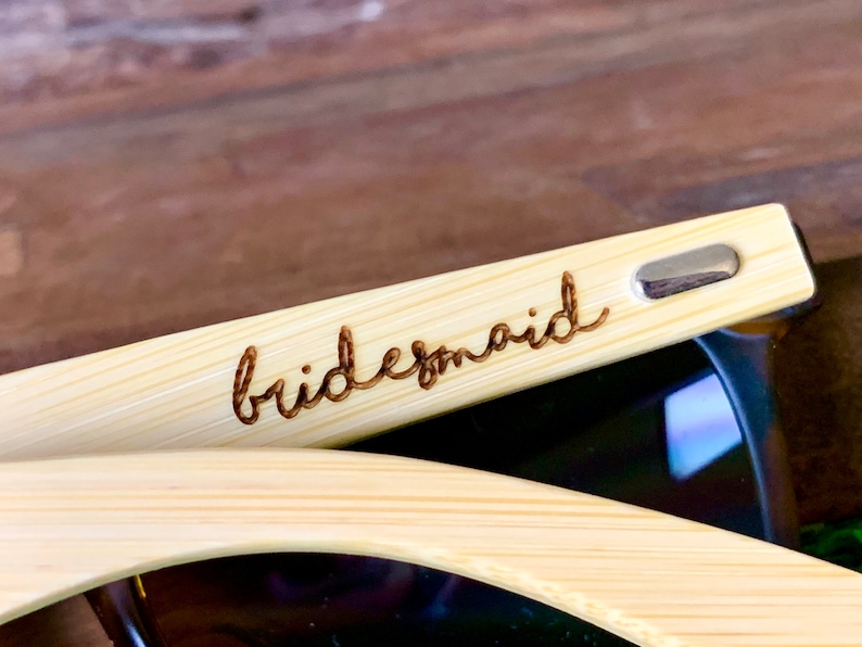 Pu&ograve; includere: Un paio di occhiali da sole in bamb&ugrave; con la parola "bridesmaid" incisa sulla montatura.