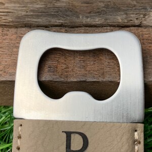 May include: A silver bottle opener with a leather strap and the letter "D" embossed on it.