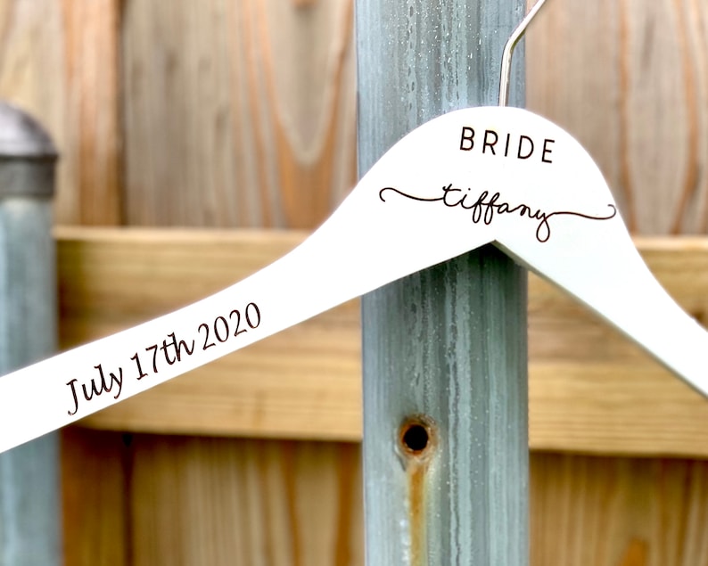 May include: White wooden hanger with the text "BRIDE tiffany" and "July 17th 2020" engraved on it.