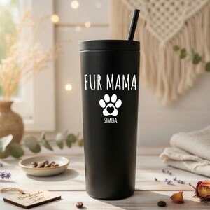 K&ouml;nnte beinhalten: Ein schwarzer Becher mit Strohhalm, mit dem wei&szlig;en Text "FUR MAMA", einem Pfotenabdruck-Design und dem Namen "SIMBA". Der Becher ist zylindrisch und vermutlich aus Edelstahl, geeignet f&uuml;r Getr&auml;nke.