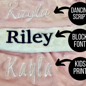 May include: Three pink and white blankets with the name "Kayla" embroidered in different styles. The top blanket has the name in a cursive script font, the middle blanket has the name in a block font, and the bottom blanket has the name in a kids print font.