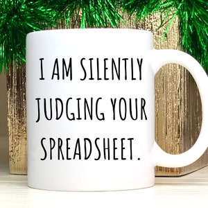 May include: White ceramic coffee mug with black text that reads "I am silently judging your spreadsheet."