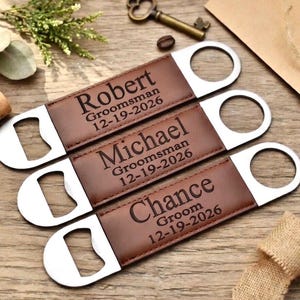 May include: Three personalized bottle openers with brown leather and silver metal. Each opener has a name and date engraved: Robert, Michael, and Chance. The text reads "Groomsman" and "Groom" respectively. A perfect gift for a wedding party.