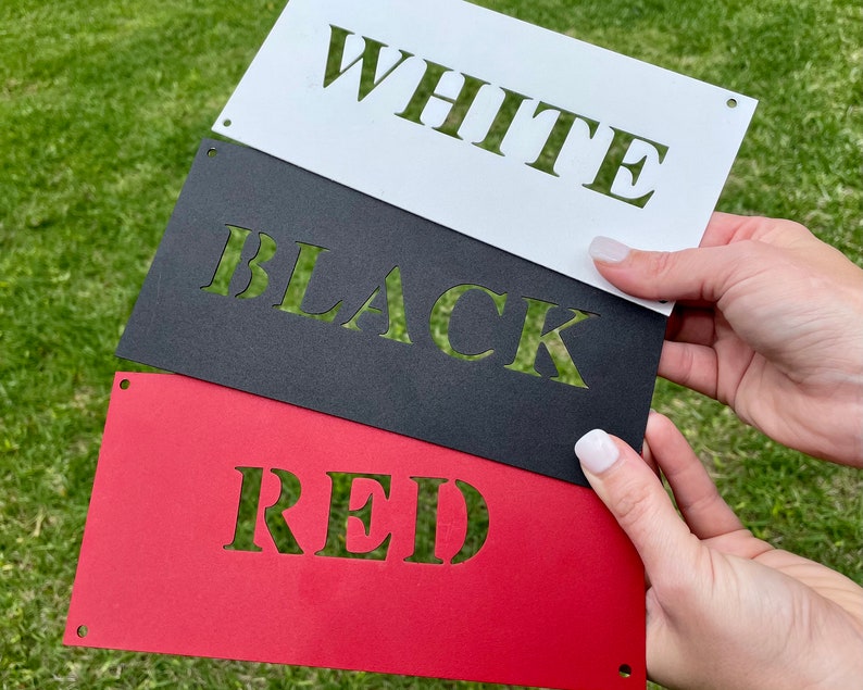 May include: Three metal signs with the words "WHITE", "BLACK", and "RED" cut out of the metal. The signs are stacked on top of each other, with the white sign on top, the black sign in the middle, and the red sign on the bottom.