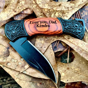 May include: A black folding pocket knife with a wood handle engraved with the message "Love you, Dad. Kendra".