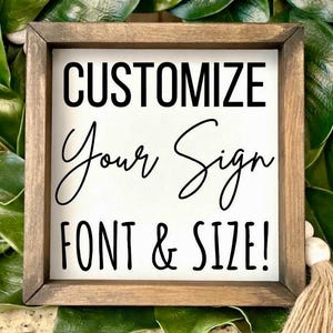 May include: A square wooden sign with a white background and a dark brown frame. The sign features the words "CUSTOMIZE Your Sign FONT & SIZE!" in black lettering. The sign is surrounded by green leaves and a tassel.