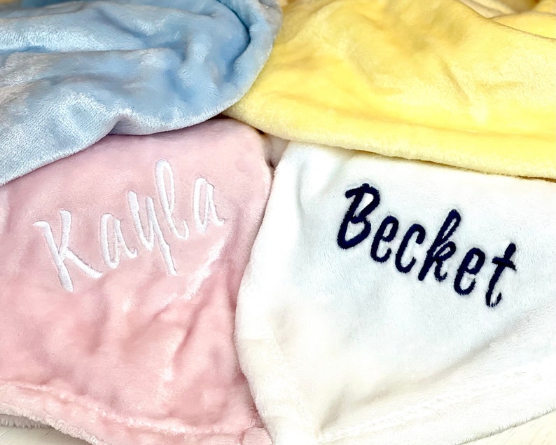 May include: Four plush blankets with embroidered names. The blankets are in shades of blue, yellow, pink, and white. The names are "Kayla", "Becket", and two others that are not visible.
