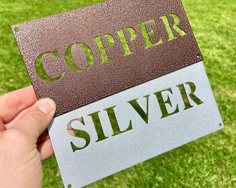 Puede incluir: Un letrero de metal con las palabras "COPPER" y "SILVER" en un esquema de colores contrastantes. La parte superior del letrero es de cobre con la palabra "COPPER" recortada en un color m&aacute;s claro. La parte inferior del letrero es de plata con la palabra "SILVER" recortada en un color m&aacute;s oscuro.