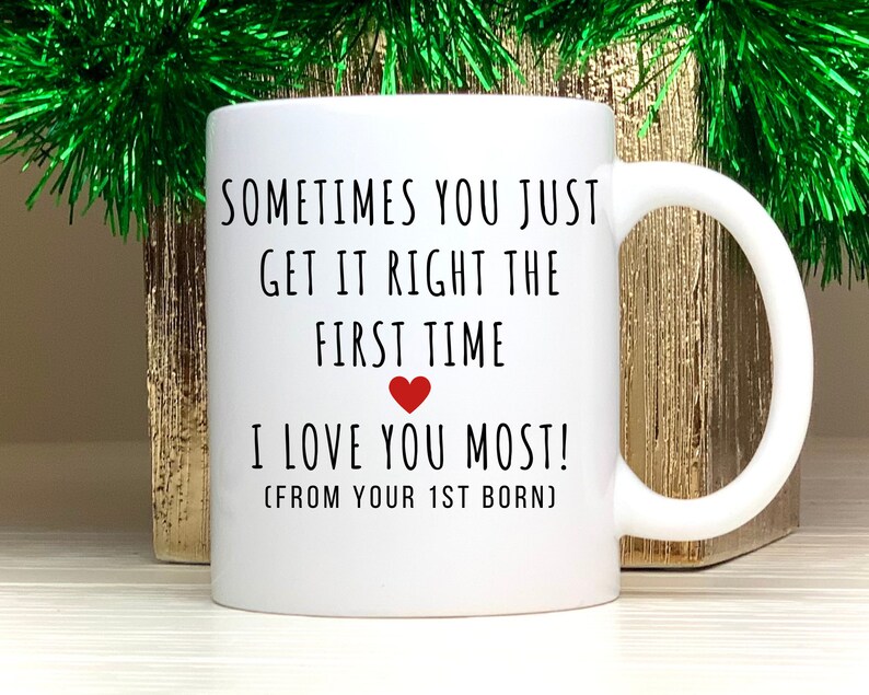 May include: White ceramic mug with black text that reads "Sometimes you just get it right the first time. I love you most! (From your 1st born)". A red heart is between the text "first time" and "I love you most!"
