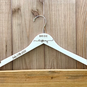 May include: White wooden hanger with the word "BRIDE" and the name "tiffany" written in cursive. The date "July 17th, 2020" is written below the name.