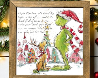 May include: A framed print with a festive illustration of the Grinch and Max. The Grinch, in green, wears a Santa hat and scarf. Max, a dog, gazes upwards. The text reads, "Maybe Christmas isn't about the lights or the gifts..."